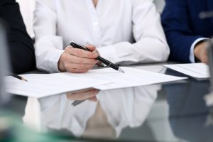 Trzy osoby siedzą przy stole, przed nimi leżą dokumenty