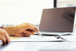 Mężczyzna robi notatki w notesie, w tle komputer