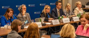 W sali konferencyjnej grupa osób siedzi przy stołach