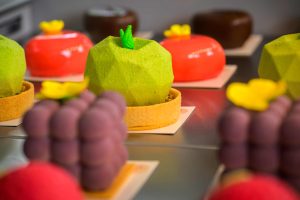 Zbliżenie na kolorowe monoporcje w kształcie owoców ustawione w witrynie cukierni Sisi Cakes.