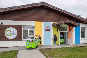 Zdjęcie budynku, w którym działa klub dziecięcy \"GórzMisie\" w Górznie. Dzieci wyjeżdżają na spacer w  kolorowych jeździkach (autkach) prowadzonych przez opiekunki.